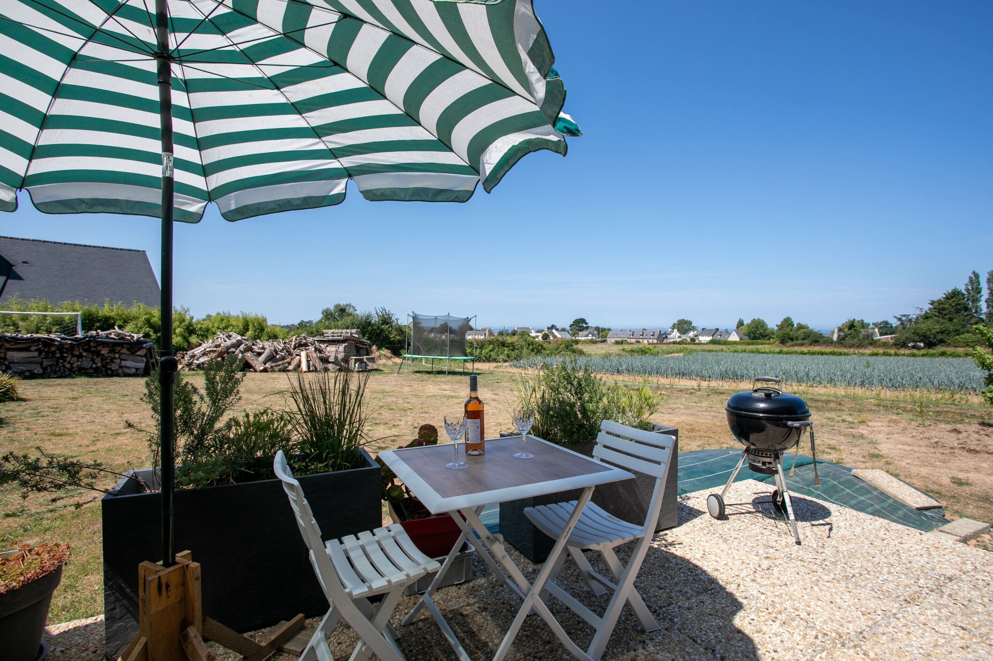 An outdoor patio with a table, chairs, a grill, and a large umbrella.
