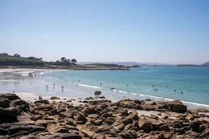 Une plage de galets bordée d’une eau d’un bleu limpide, quelques personnes qui se baignent et des collines qui se dessinent à l’horizon.