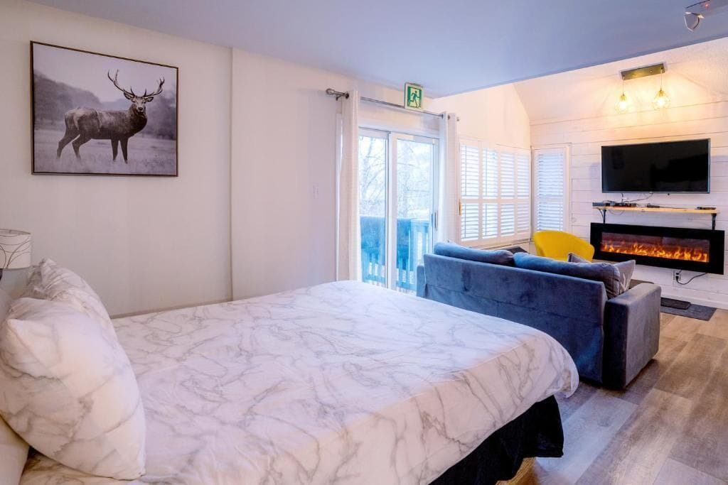 Un dormitorio con una cama grande, televisión, chimenea y balcón con vistas.
