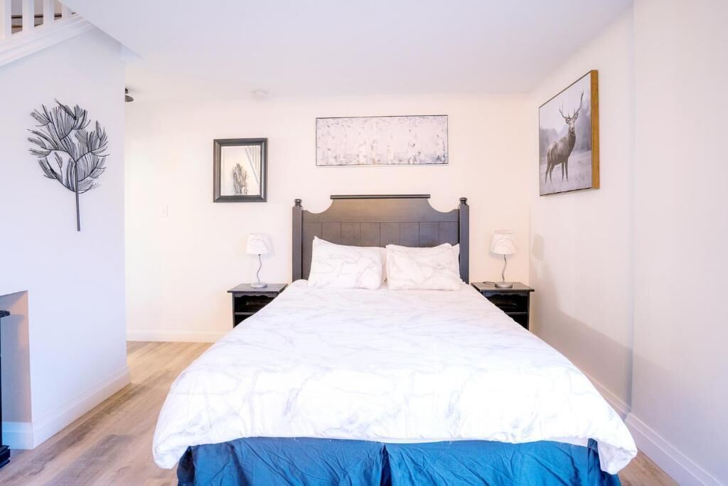 A bedroom with a large bed, two bedside tables, a framed picture, and a wall-mounted artwork.
