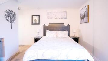 A bedroom with a large bed, two bedside tables, a framed picture, and a wall-mounted artwork.