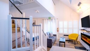 Una sala de estar moderna con una escalera, un sofá, un sillón amarillo, una chimenea y un televisor.