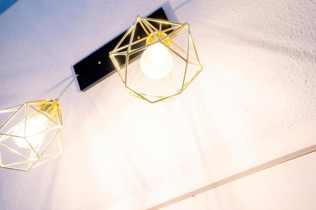 Dos lámparas colgantes geométricas con bombillas expuestas sobre una pared blanca.