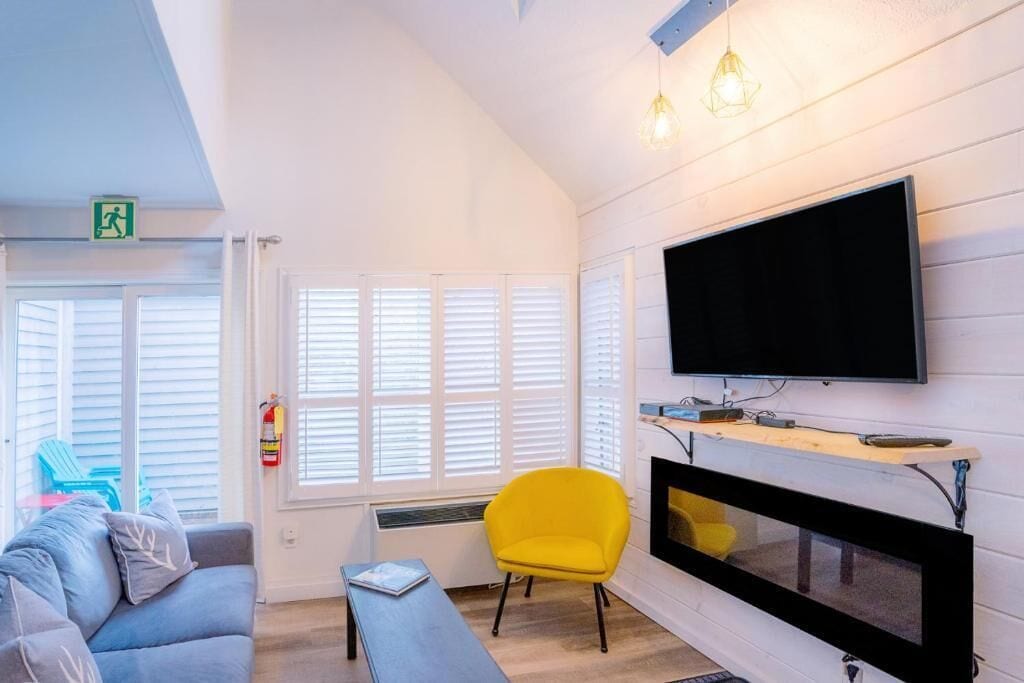 A modern living room with a flat-screen TV, a yellow armchair, and a grey sofa.