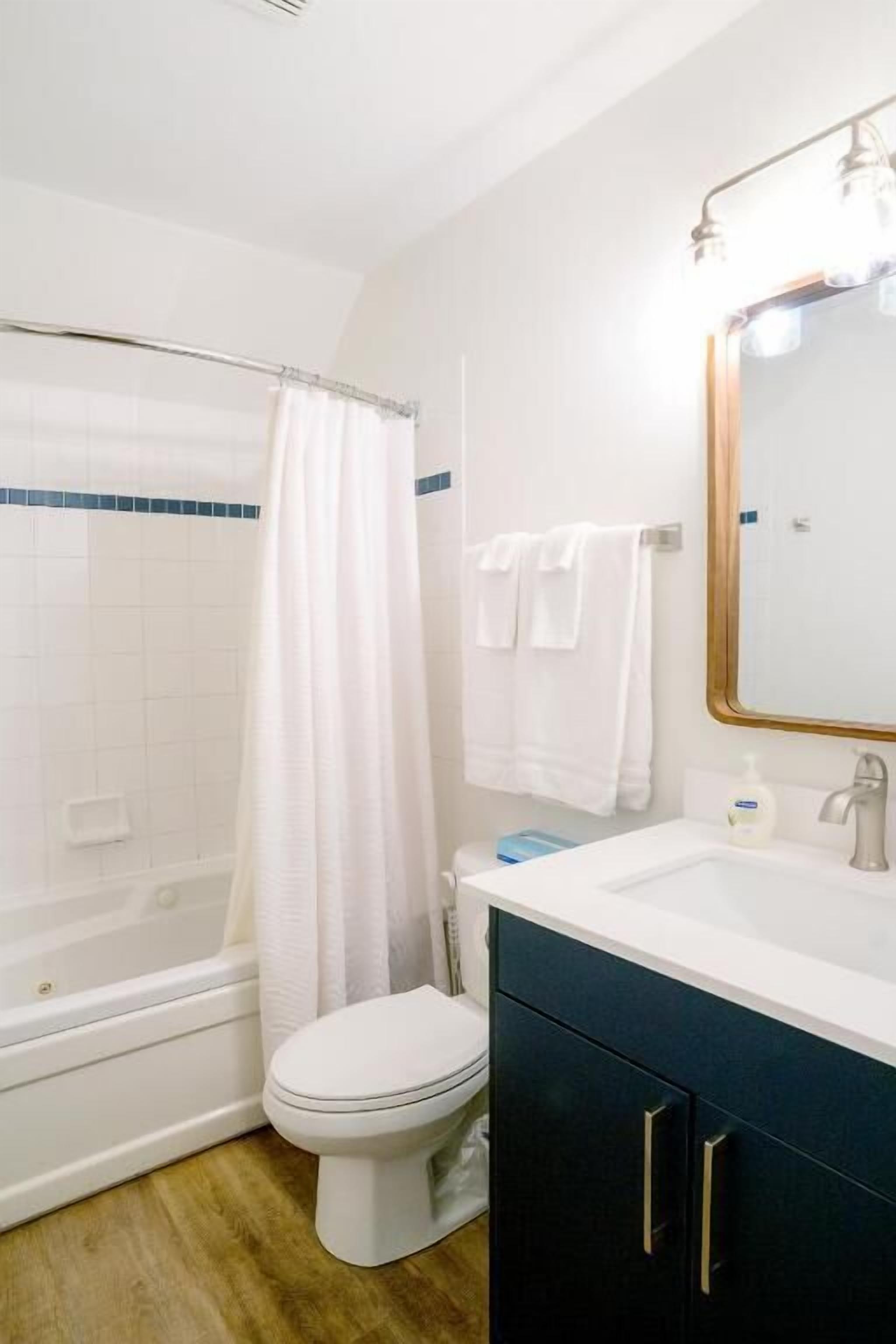 A bathroom with a bathtub, toilet, and vanity with a mirror.