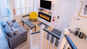 Una sala de estar moderna con un sofá, un sillón amarillo, una chimenea, un televisor y una escalera.