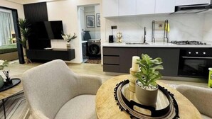 Un salon moderne comprenant un canapé, une table basse agrémentée d’objets décoratifs, et un coin cuisine avec une cuisinière, un évier et des placards.