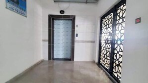 A hallway with a tiled floor, a door with a grid pattern, and a decorative black gate on the right.
