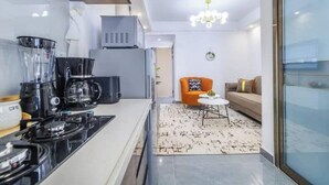 A modern kitchen with a coffee maker, a microwave, and a stove. There is a small round table with a chair in the living area.