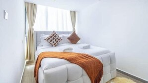 A modern bedroom with a large bed, white bedding, and a window with curtains.