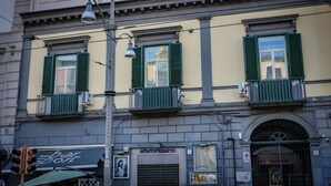 Um edifício com três janelas, cada uma com persianas verdes, uma placa com a inscrição "effettomassimo" e um portão de metal fechado na entrada.