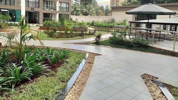 Un immeuble d’appartements moderne doté d’une cour aménagée comprenant une terrasse, un espace salon et un petit élément décoratif aquatique.