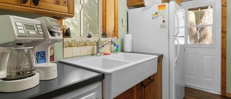 Una cocina con armarios de madera, un refrigerador blanco, una cafetera y un lavamanos.