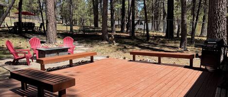 Eine Holzterrasse mit Bänken und roten Adirondack-Stühlen, umgeben von Bäumen.