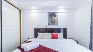 Una habitación de hotel con una cama, cabecera, un cuadro en la pared y una colcha roja sobre la cama.