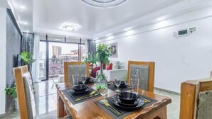 Un comedor con una mesa de madera dispuesta para cuatro personas, una planta en maceta y vistas de la ciudad a través de amplios ventanales.