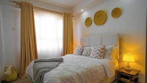 A bedroom with a bed, curtains, a bedside lamp, and decorative plates on the wall. - Kilimani One bedroom (Nairobi)