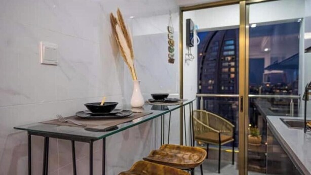 A modern kitchen with a glass partition, a dining table with chairs, and a view of the city at night. - Kilimani One bedroom (Nairobi)