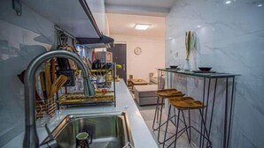 A modern kitchen with a stainless steel sink, a dish rack, and a bar stool. - Kilimani One bedroom (Nairobi)
