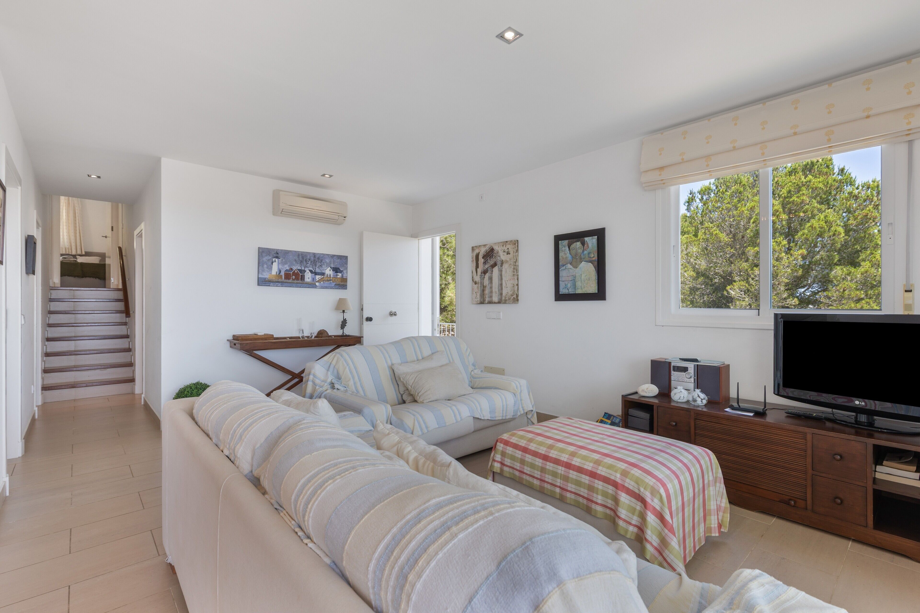 A spacious living room with a sofa, a television, and a staircase leading to another room.