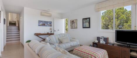 A spacious living room with a sofa, a television, and a staircase leading to another room.