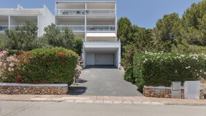 A multi-story building with a garage entrance, surrounded by greenery and stone walls. - Apartment 'Infinity View Menorca' with Sea View, Shared Pool and Private Terrace (Es Mercadal)