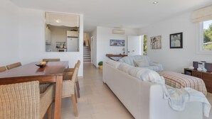 A modern interior with a dining area, sofa, and a staircase leading to a kitchen. - Apartment 'Infinity View Menorca' with Sea View, Shared Pool and Private Terrace (Es Mercadal)