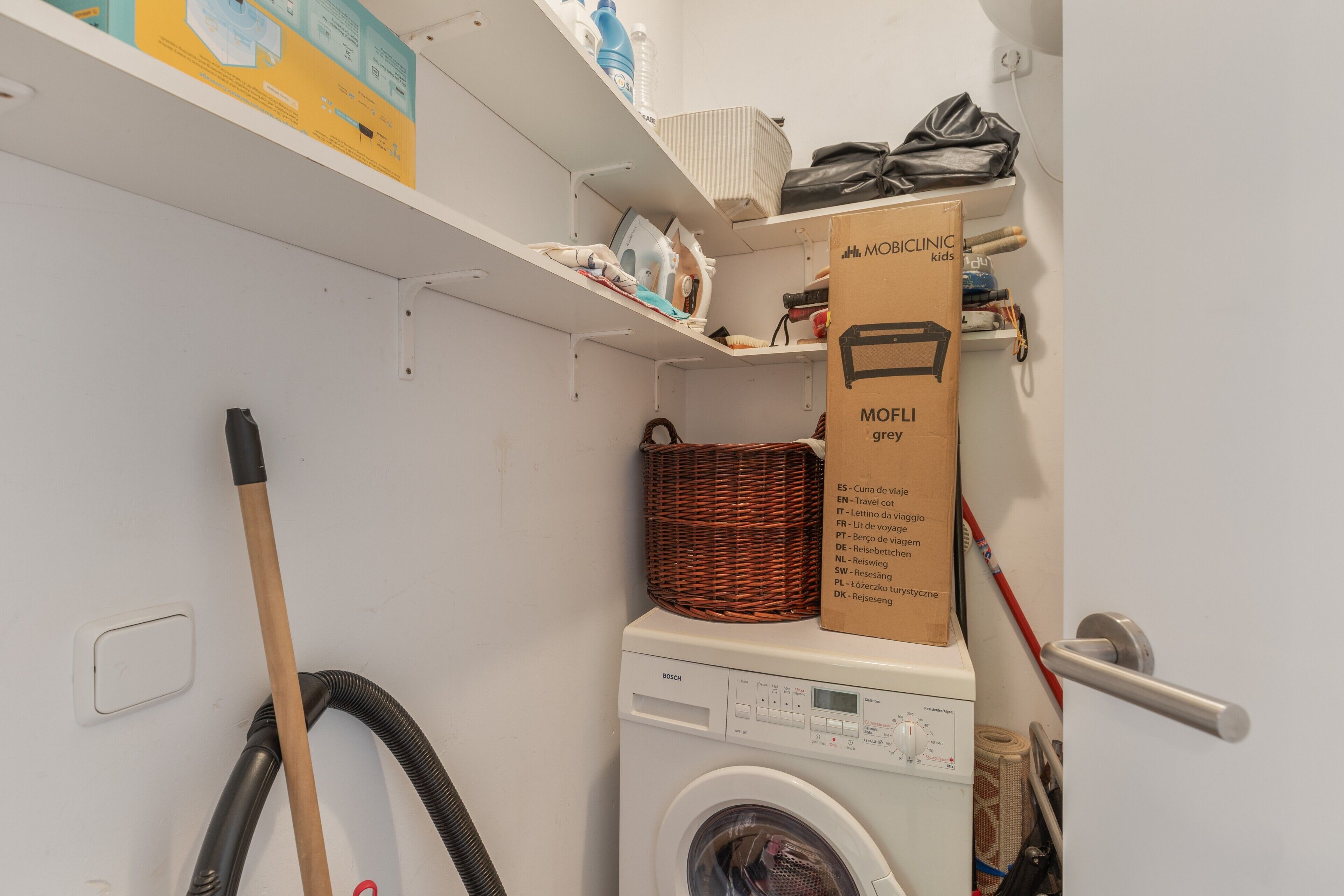 A laundry room with a Bosch washing machine, a wicker basket, and a cardboard box labeled 'MOBICLINIC kids.'