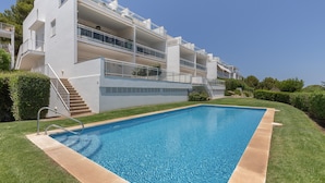 A modern building with a swimming pool, balconies, and a clear sky. - Apartment 'Infinity View Menorca' with Sea View, Shared Pool and Private Terrace (Es Mercadal)