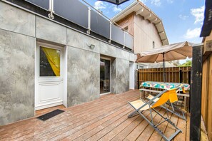 A modern building with a wooden deck, a covered outdoor seating area, and a window with a yellow curtain. - Studio Abygaelle with Terrace – Comfort and Tranquility in Lège-Cap-Ferret (Lège-Cap-Ferret)