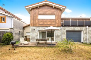 A modern house with a patio, a barbecue grill, and a dining table.