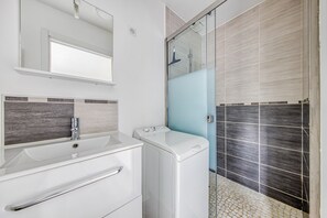 A modern bathroom with a white sink, a mirror, a glass shower enclosure, and a tiled floor.