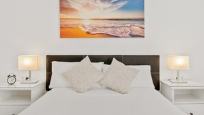 A bedroom with a large bed, two bedside tables with lamps, a clock, and a beach scene painting on the wall. - Apartment 'Fuengirola Beach' with Sea View, Wi-Fi and Air Conditioning (FUENGIROLA)