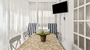 A room with a TV mounted on the wall, a table with a patterned tablecloth, striped chairs, and a potted plant. - Apartment 'Fuengirola Beach' with Sea View, Wi-Fi and Air Conditioning (FUENGIROLA)