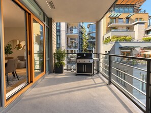 A balcony with a grill, a dining area with chairs and a table, and a potted plant.