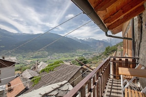 Un balcon doté d’une table et de chaises en bois, offrant une vue sur un paysage montagneux parsemé de bâtiments traditionnels.