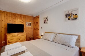 Une chambre d’hôtel avec un mur en bois, un téléviseur à écran plat, un lit avec une literie blanche et une œuvre d’art représentant un scooter accrochée au mur.