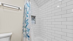 Une salle de bain avec des murs carrelés de carreaux blancs, une baignoire blanche et un rideau de douche orné d’un motif de feuilles.