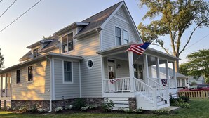 Une maison à deux étages avec un porche, un drapeau et des fondations en pierre.