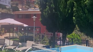 Una piscina con sillones de descanso, un farol y un edificio rojo al fondo.