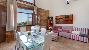 Un salón con una mesa de vidrio, sillas blancas, un sofá a rayas rosadas y una estantería.