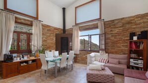 Amplia sala de estar con pared de piedra, chimenea, una mesa de comedor con sillas, sofá y estantería.