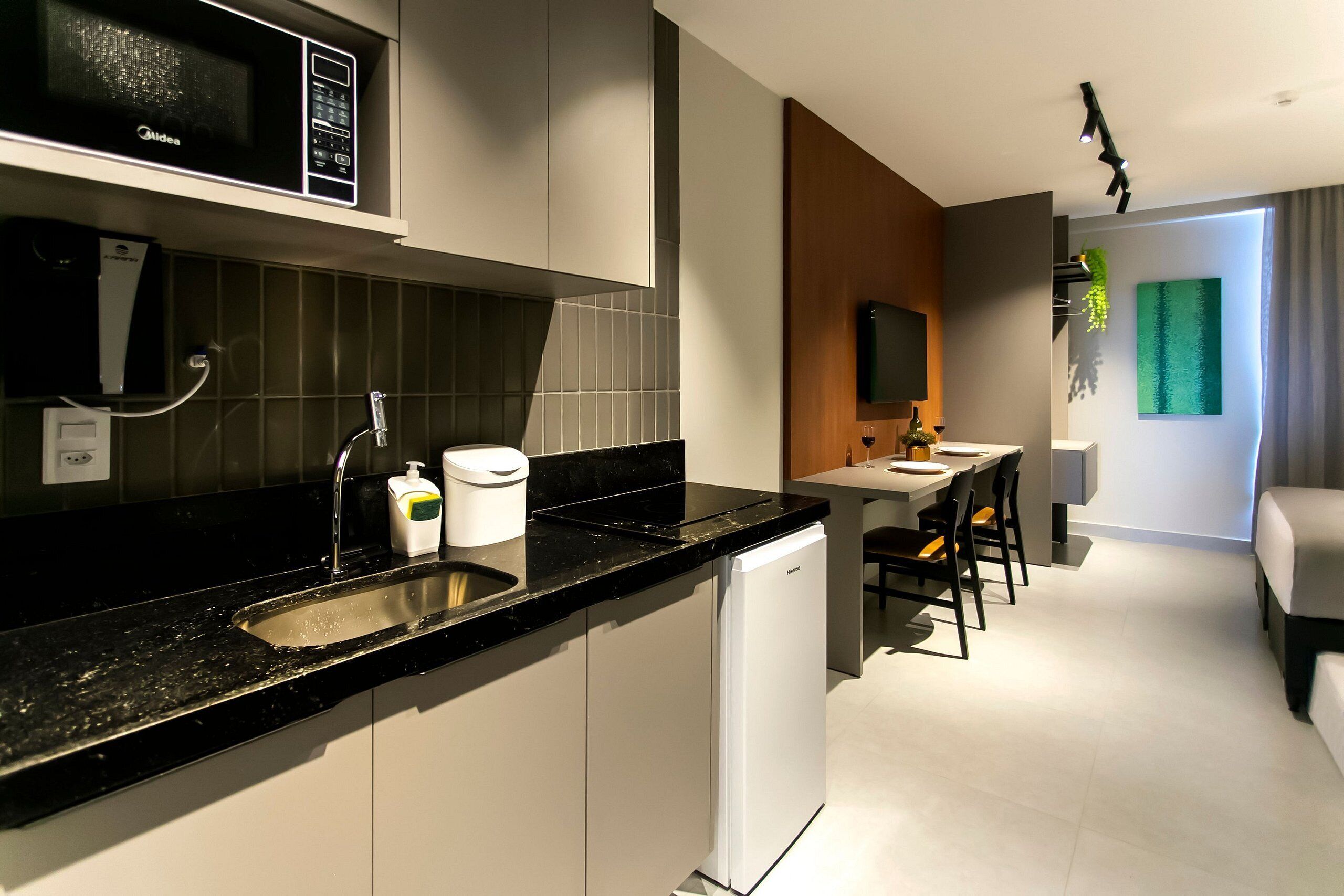 Una cocina moderna con encimera negra, armarios blancos y microondas integrado. Cuenta con un comedor con mesa y sillas, además de una pequeña zona de estar con sofá.