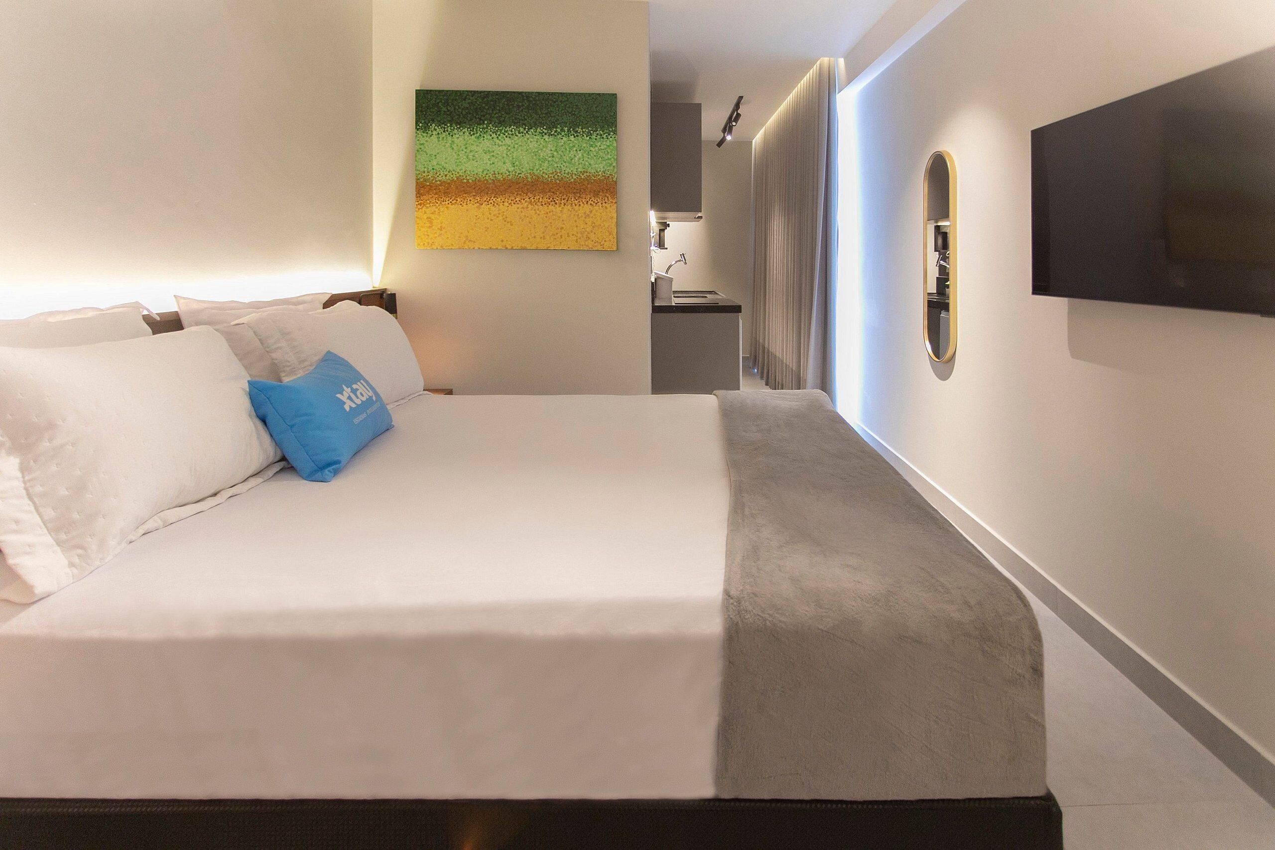 Ein Hotelzimmer mit Bett, einem Gemälde, einem Fernseher und einer kleinen Küchenzeile.