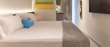 Ein Hotelzimmer mit Bett, einem Gemälde, einem Fernseher und einer kleinen Küchenzeile.
