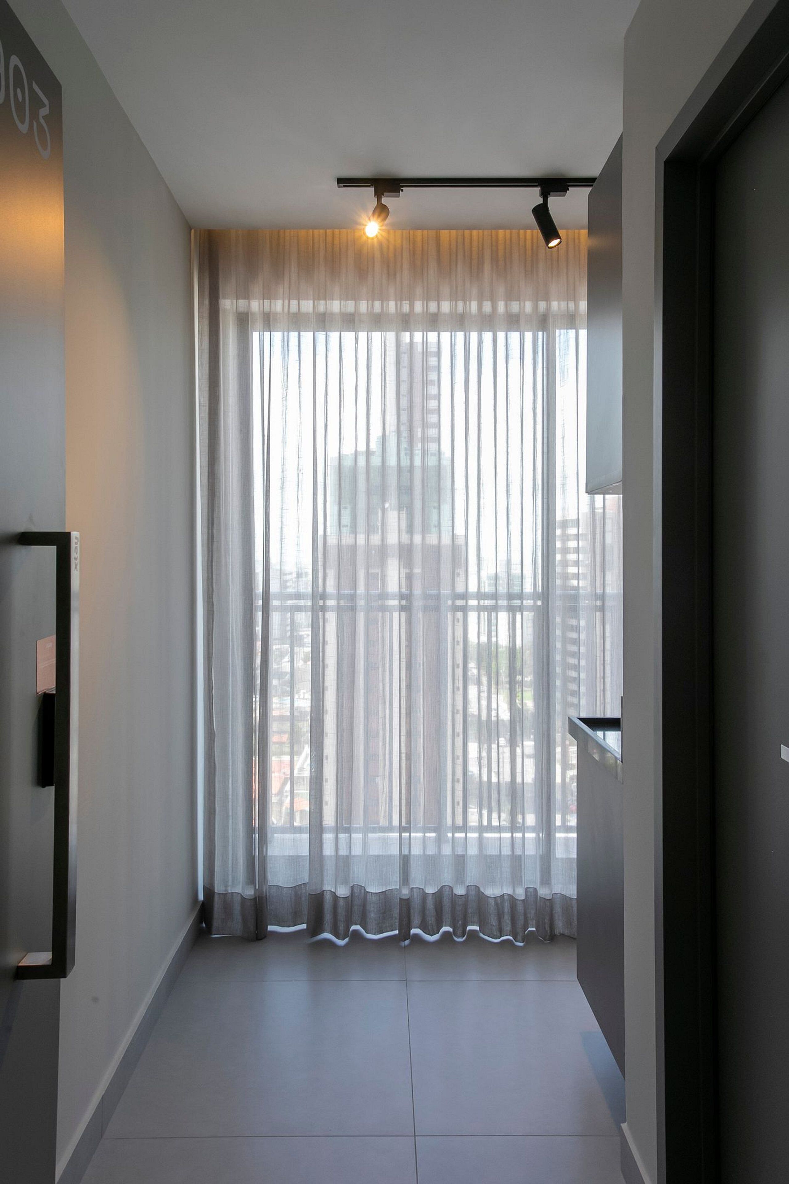 A modern hotel room with a large window, sheer curtains, and a ceiling-mounted light fixture.