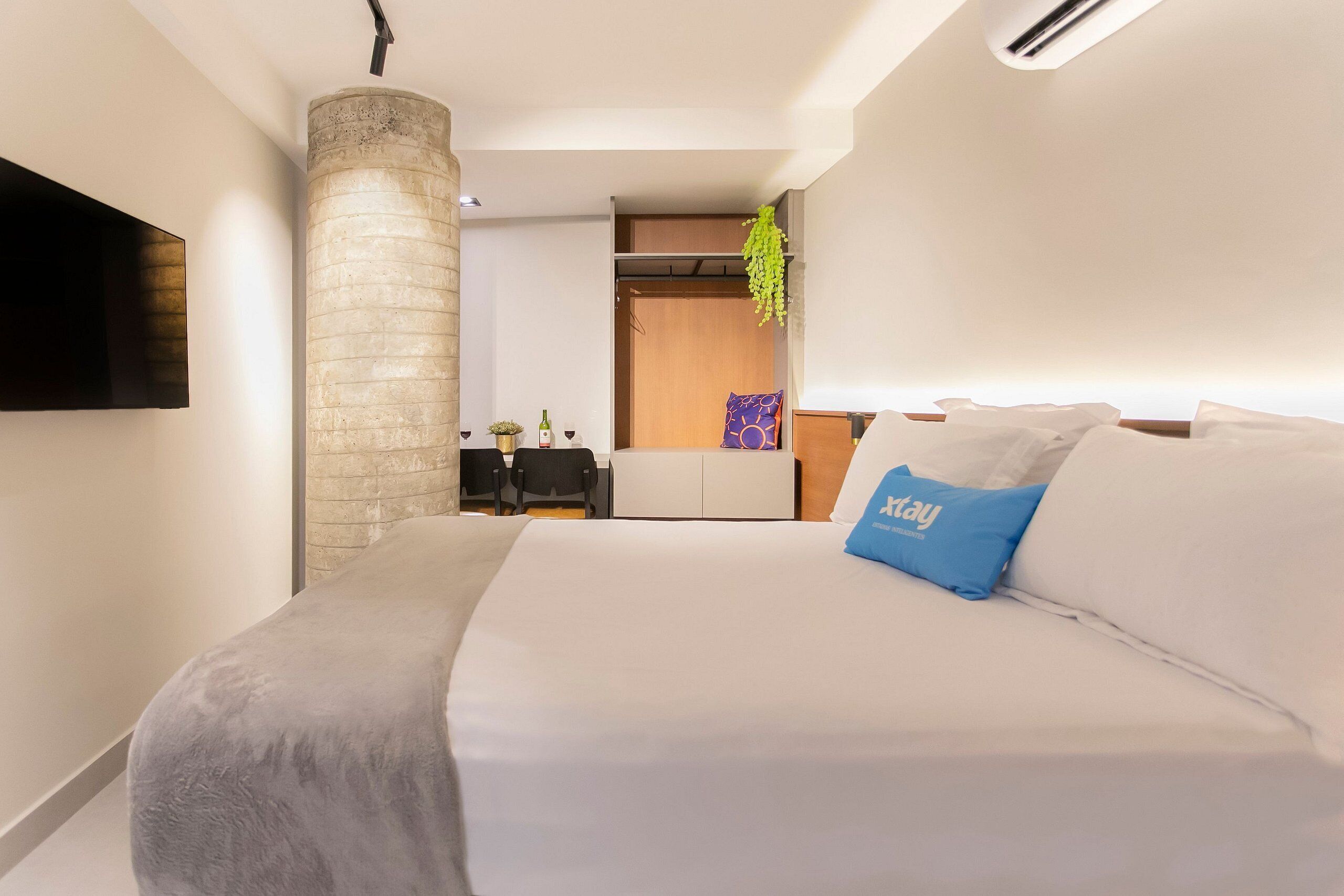 Habitación de hotel moderna con una cama grande, un televisor de pantalla plana en la pared, un pilar de piedra y un escritorio pequeño con una silla.