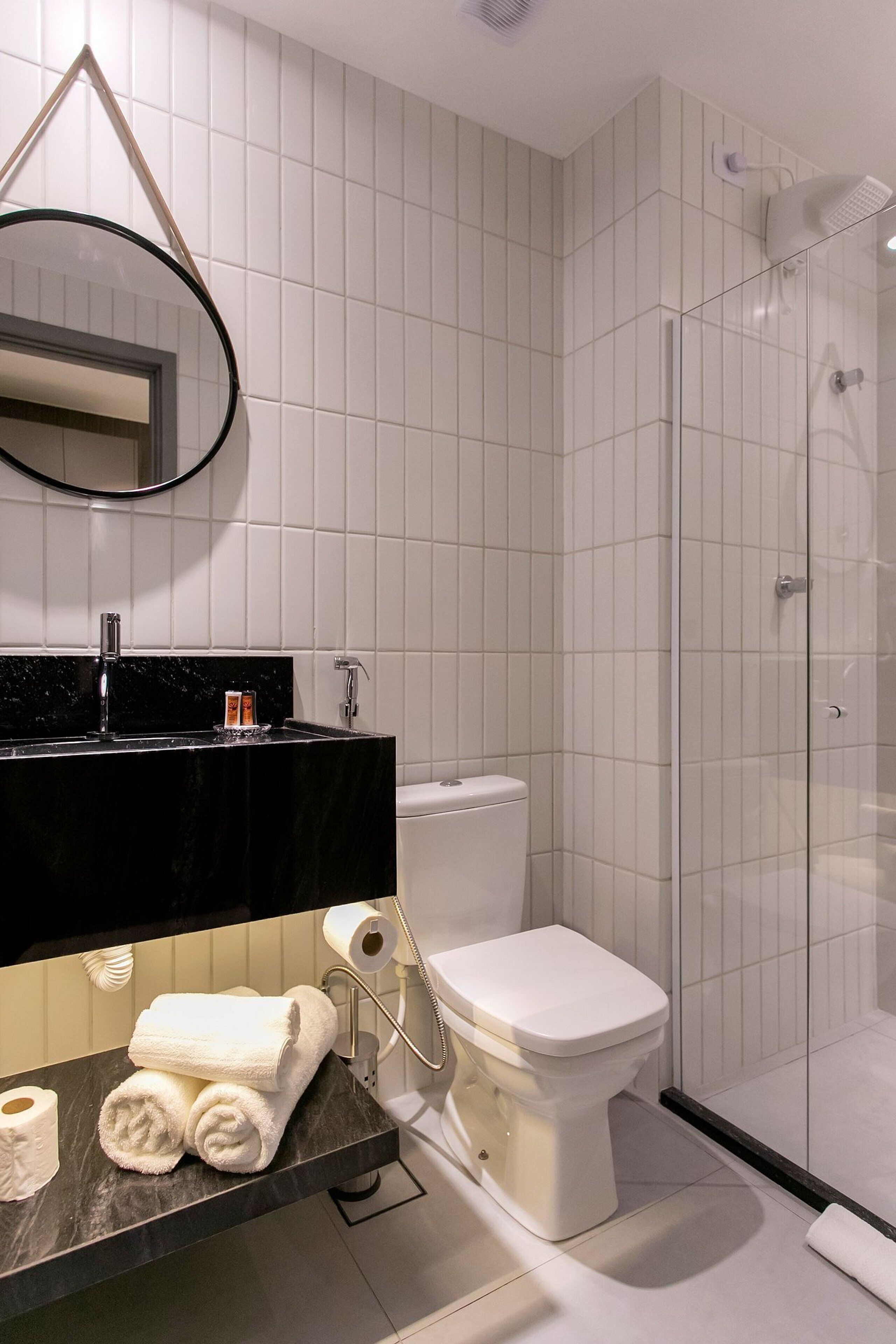 Ein modernes Badezimmer mit schwarzem Waschtisch, weißen Fliesen, einer Duschkabine aus Glas und einer Toilette.