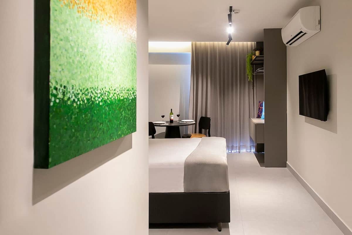 Ett modernt hotellrum med en stor, abstrakt målning, en säng, ett skrivbord, en stol, en tv och en luftkonditioneringsanläggning.