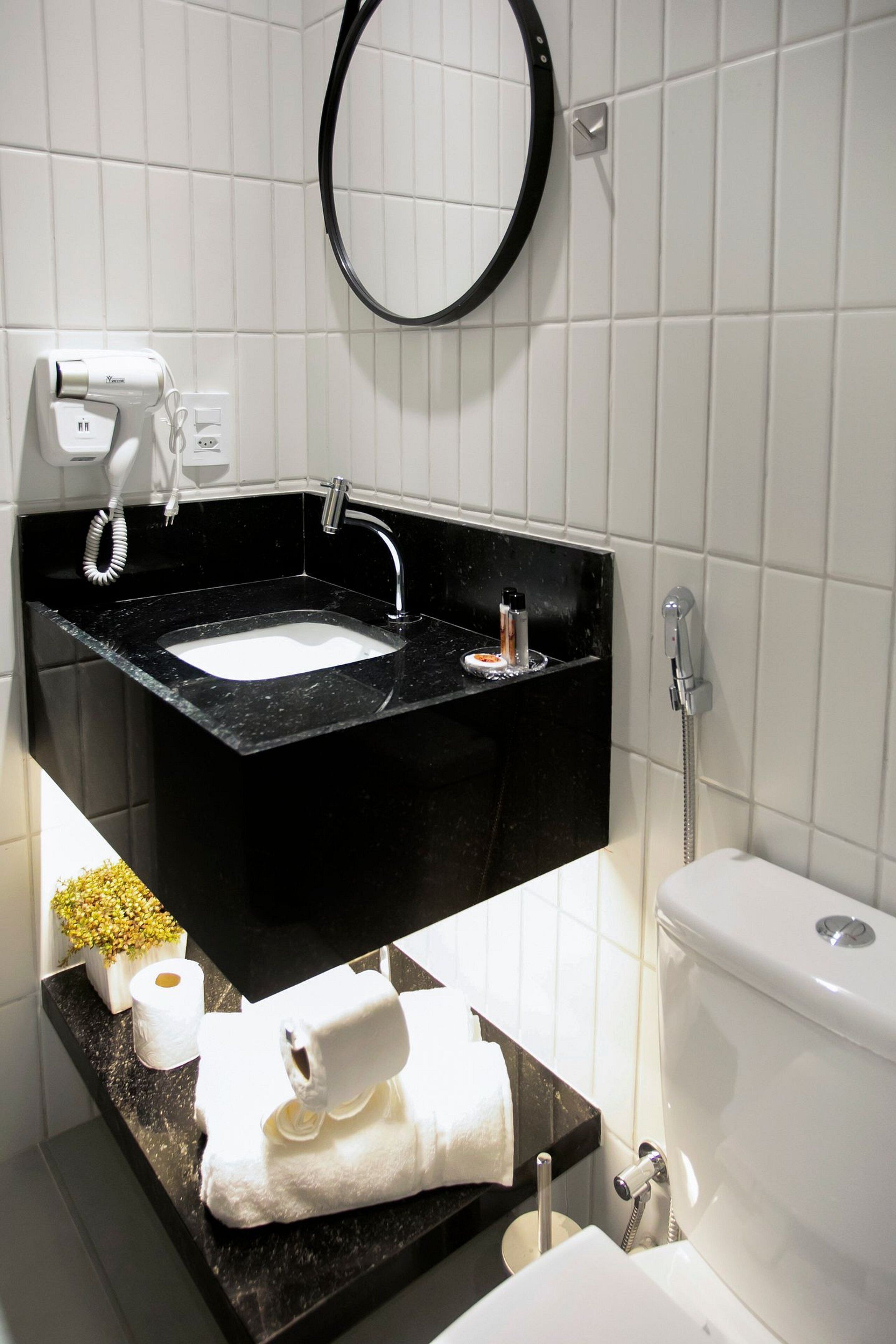 A bathroom with a black sink, white tiles, a toilet, and a hairdryer on the counter.